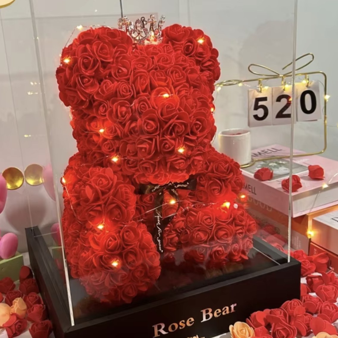 Urso feito de rosas vermelhas, com coroa, luzes e fita Just for you, dentro de uma caixa de acrílico sobre a base escrita Rose Bear